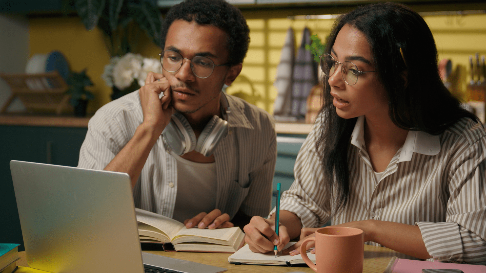 A man and woman looking at a laptop screen and taking notes in a notebook