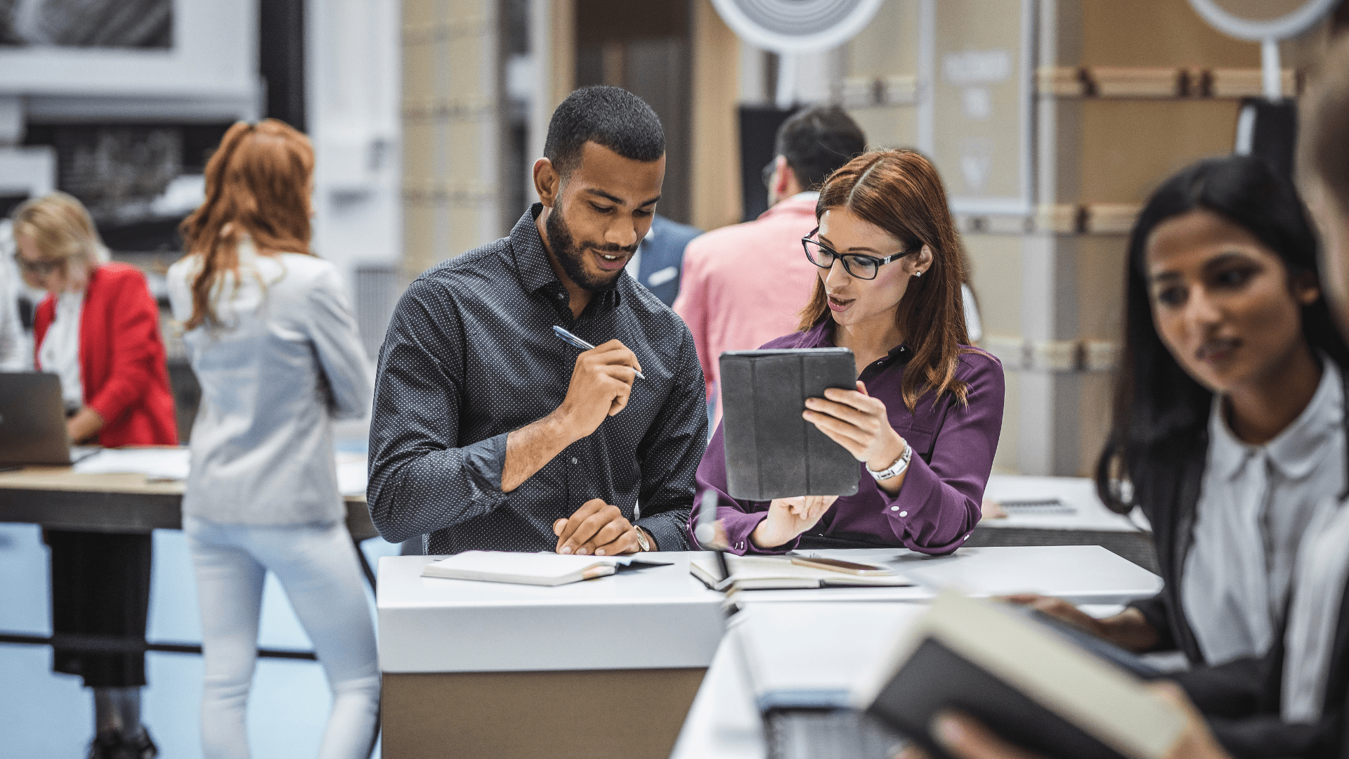 A man and woman stood at a table looking at a tablet device and making notes in a notebook
