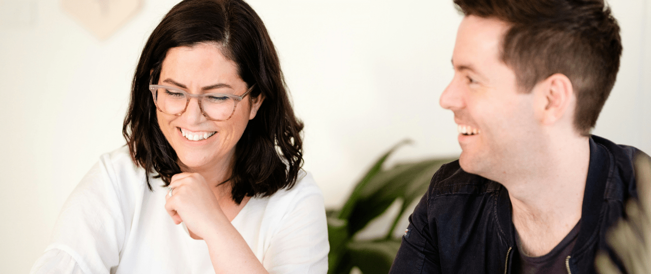 A man and woman sat next to each other smiling and looking at a computer