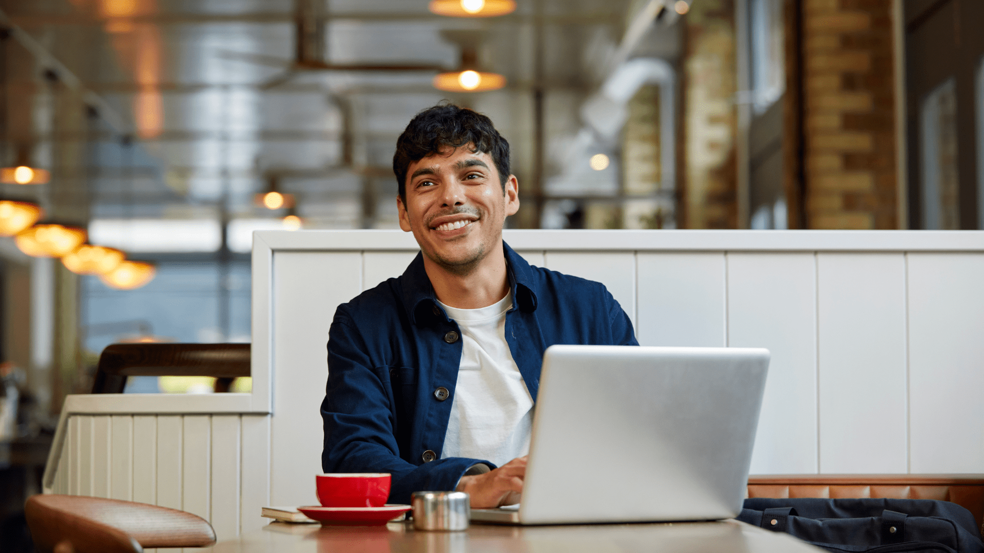 A man smiling while sitting at a table on his laptop