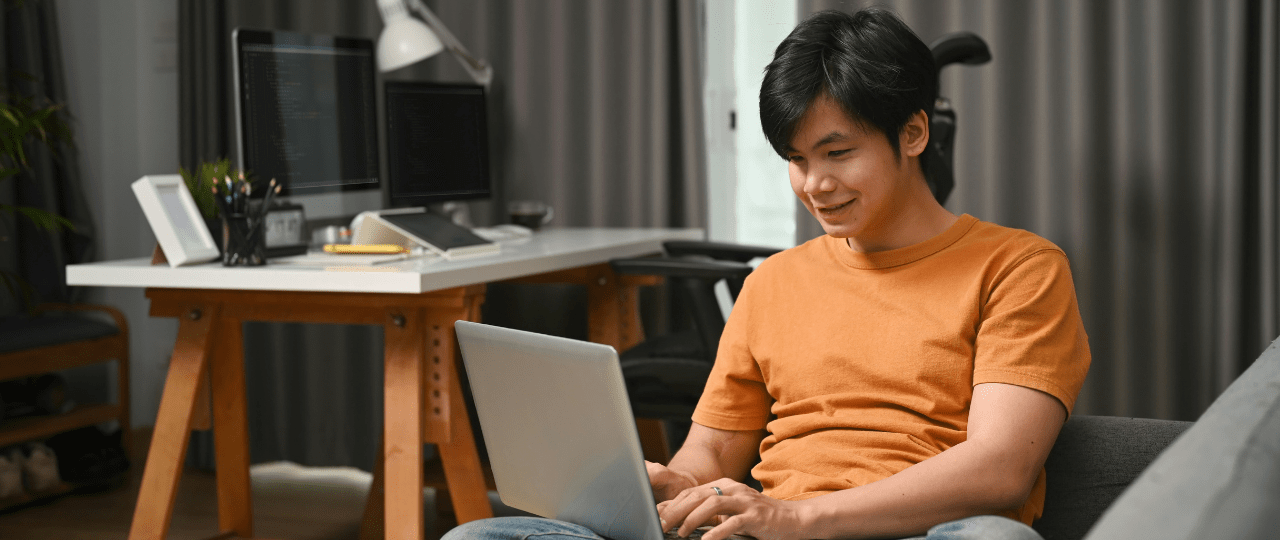 Young man sat on a sofa smiling while working on his laptop