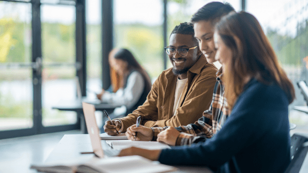 A group of students smiling and in conversation huddled around a computer
