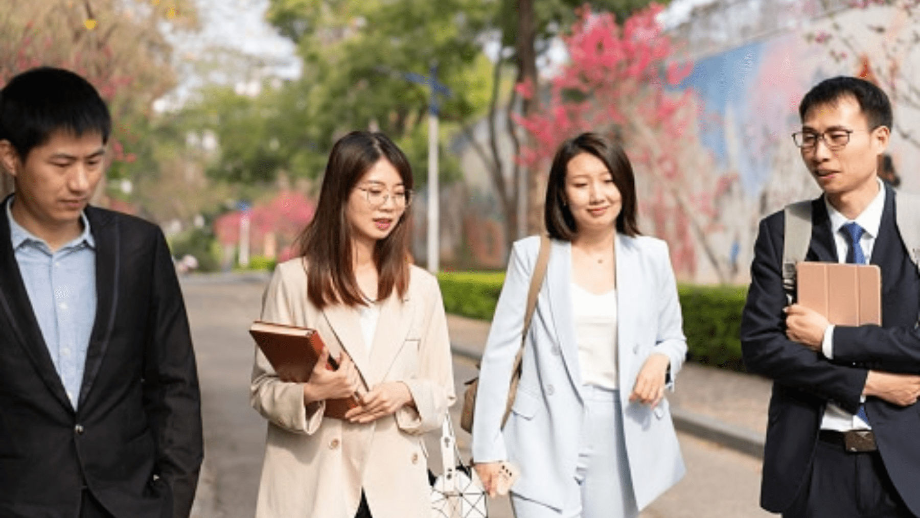 Four Asian students walking and talking while carrying books