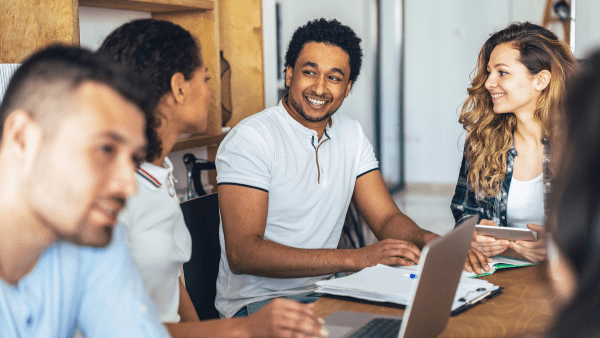 A group of young people sat at a table smiling and in discussion
