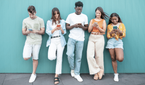Five teenagers on their phones resting against a blue wall