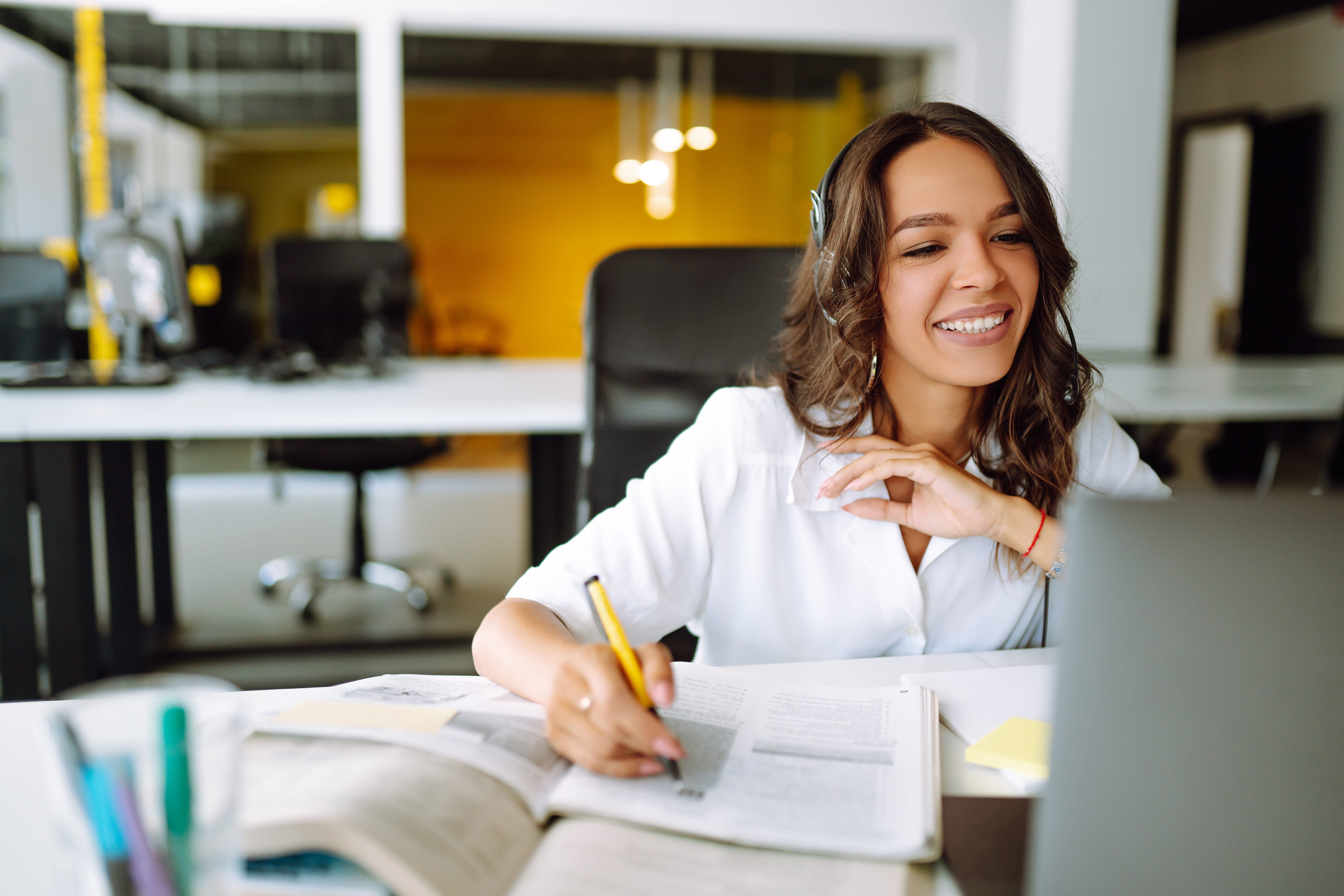 Woman smiling while looking at her computer and writing something on a notepad