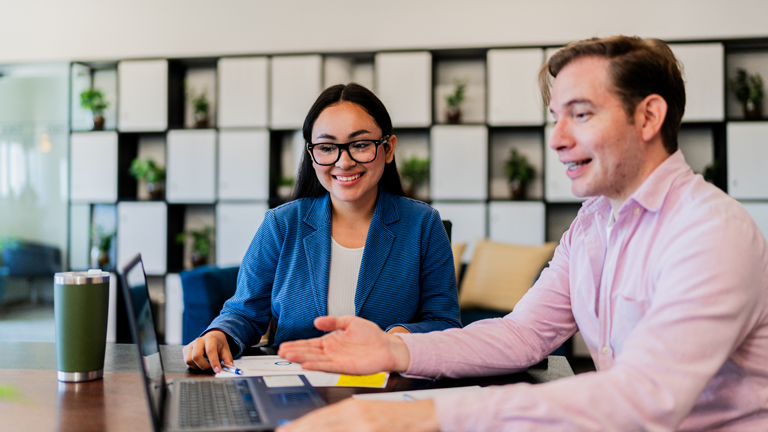two colleagues sitting at desk collaborating over laptop
