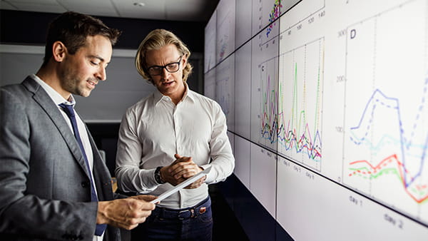 two-men-looking-at-complex-data-on-large-screen-in-dark-room