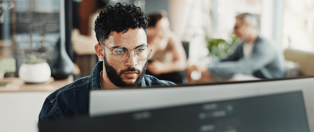 Man looking at a computer with people talking behind him