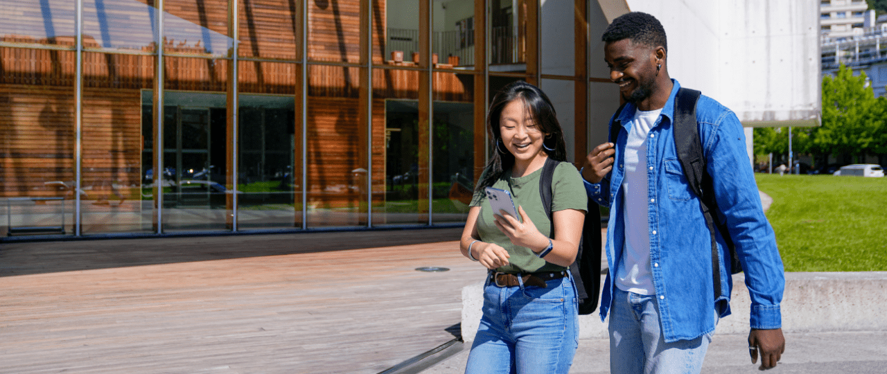 Two college students walking across campus looking at a phone while smiling