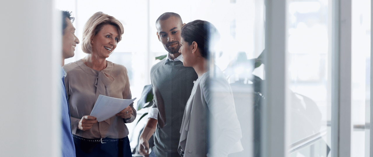 A group of four people are talking while smiling and looking at a document