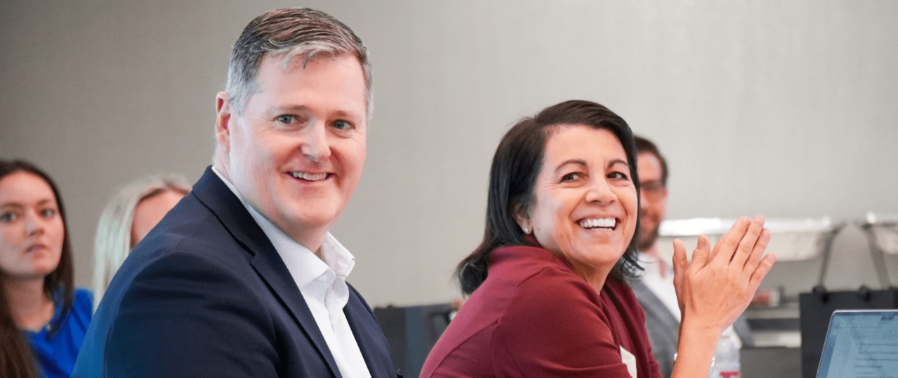 A man and woman at a conference smiling and looking over to their right