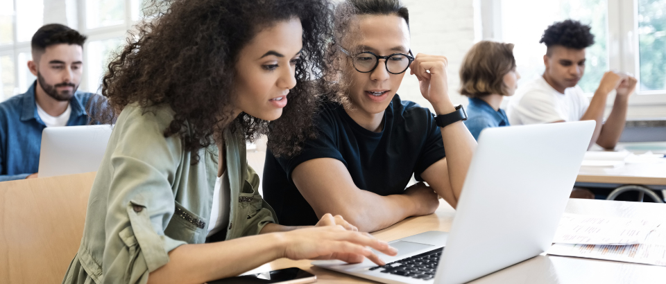 Two people sitting at a desk looking at a laptop screen together