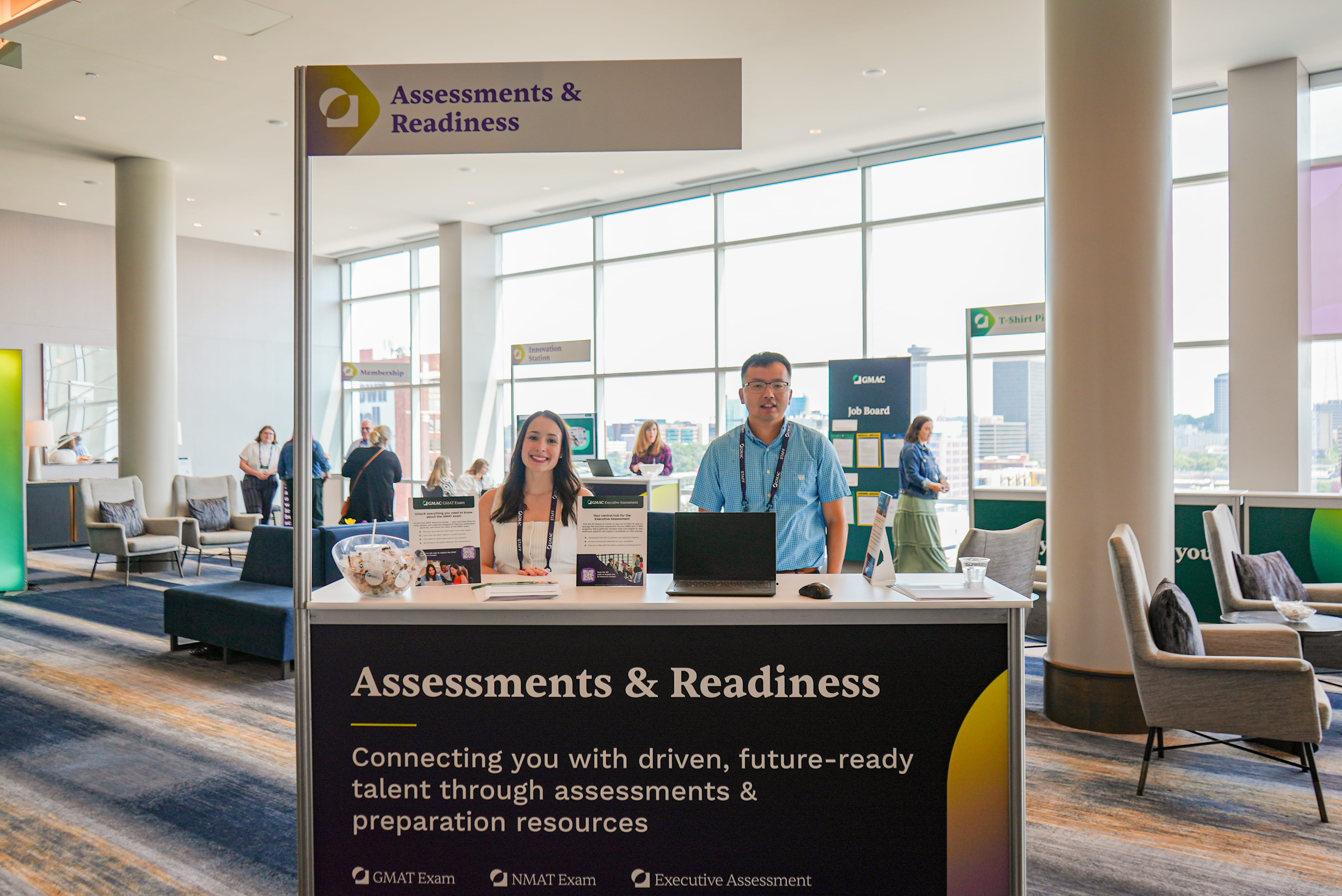 Man and woman stand behind a booth that says "Assessments and Readiness"
