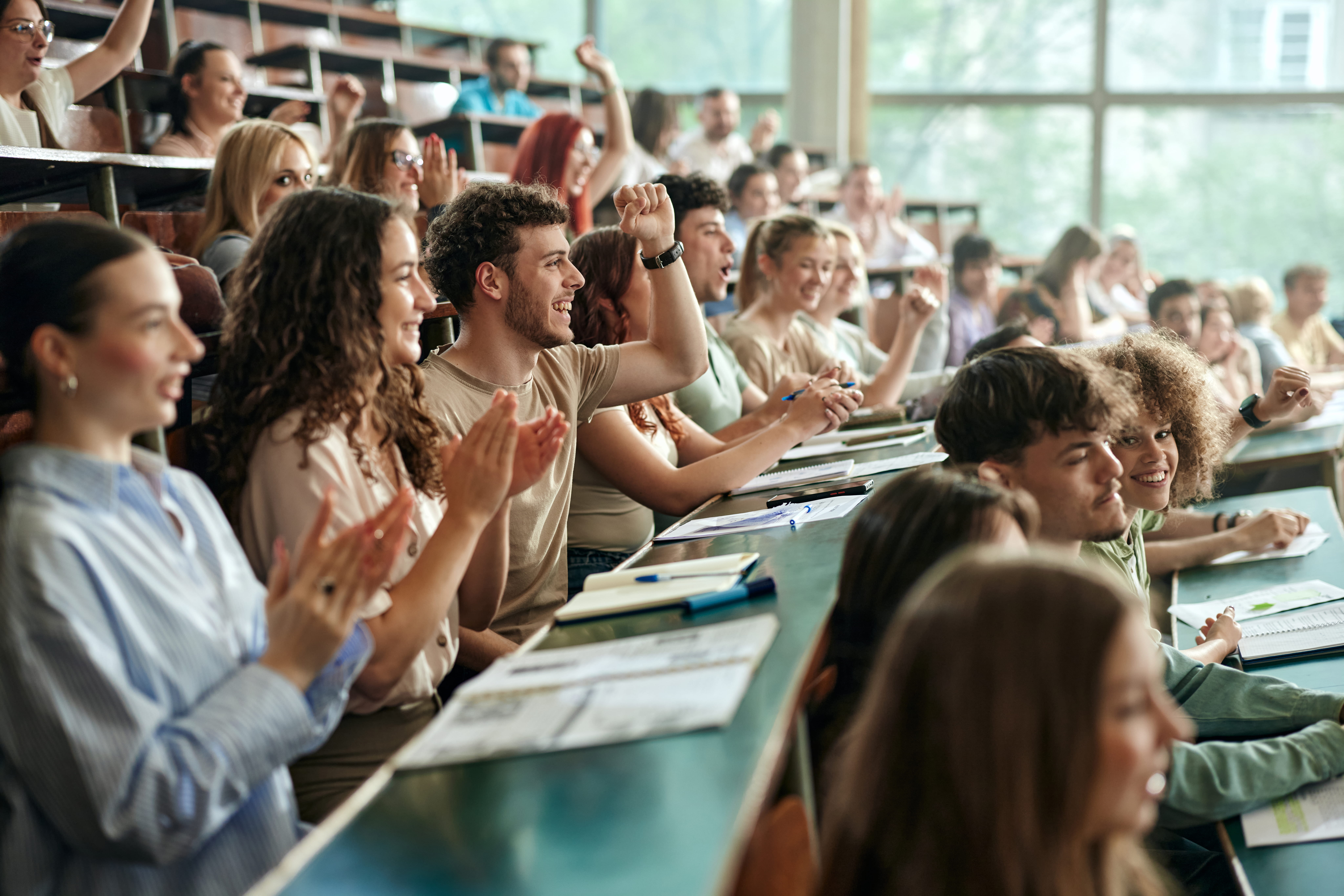 Students raise hands in lecture style classroom
