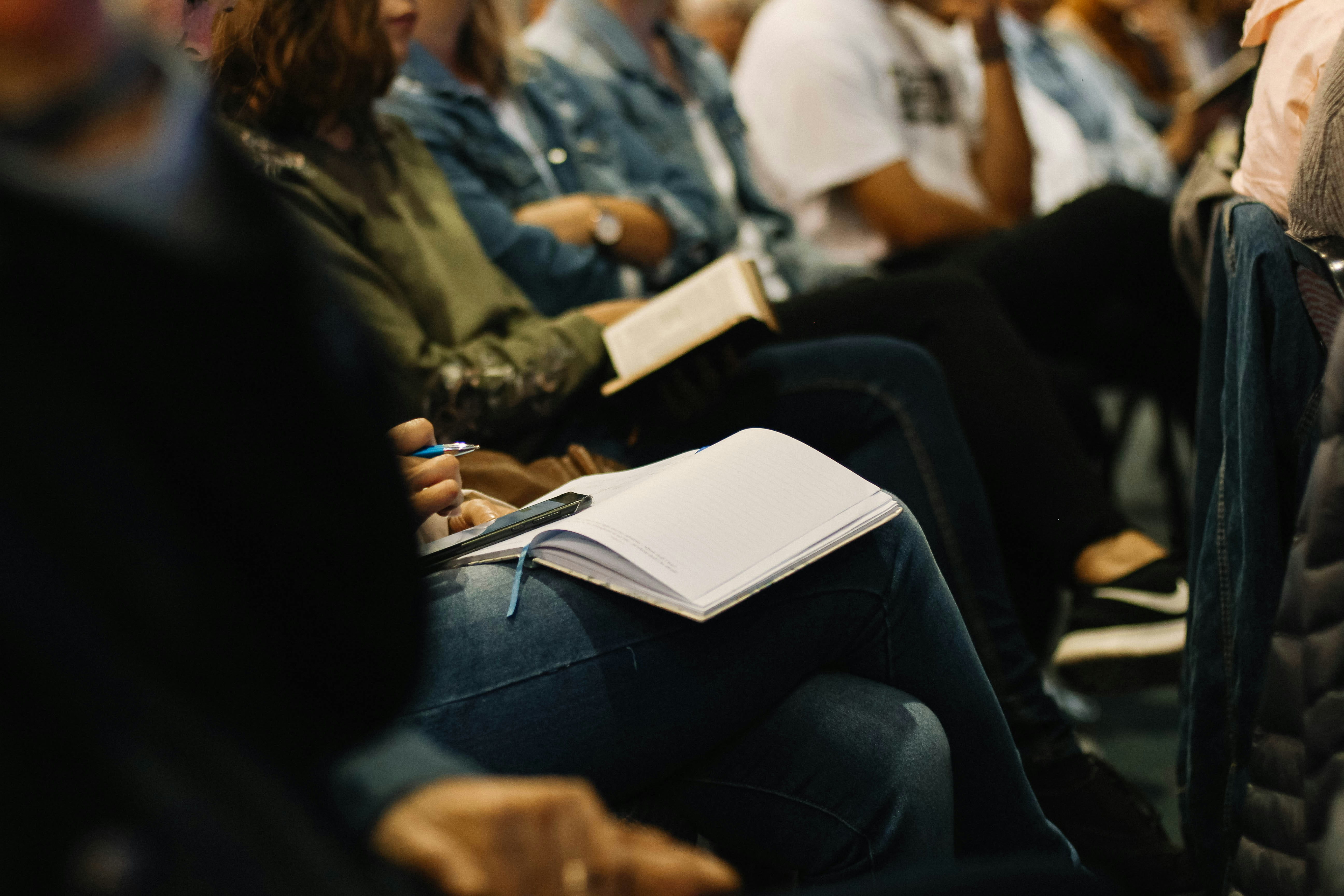 A blank notebook on the lap of a person sitting in a lecture hall