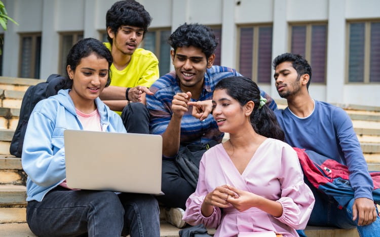 A group of students sitting on stairs and looking at a laptop screen