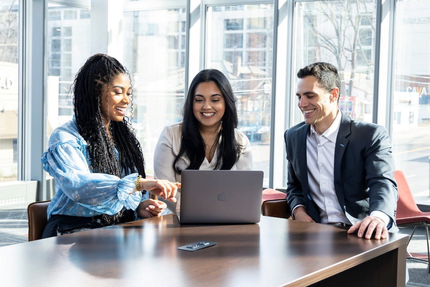 Three smiling professionals sitting in a modern office in front of a laptop together